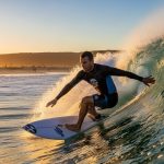 Man wearing a long sleeve rash guard while surfing a wave at the beach