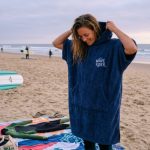 Person wearing a surf poncho changing robe on a sandy beach after a surf session