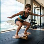 Surfer training core strength on a balance board in a modern gym.