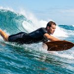 Surfer carving a blue ocean wave using a wooden handplane.